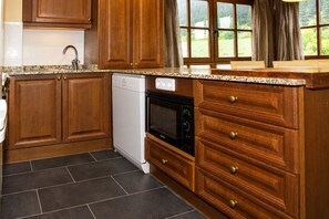 Une cuisine avec des meubles de rangement en bois, un lave-vaisselle, un four et une fenêtre avec des rideaux.