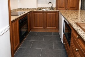 Une cuisine avec un carrelage foncé, des meubles en bois, un évier en acier inoxydable et un lave-vaisselle.