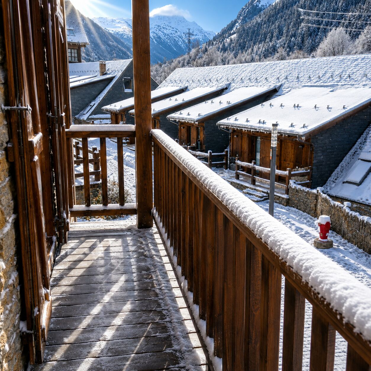 A wooden balcony with a snow-covered roof, overlooking a mountainous landscape with buildings.