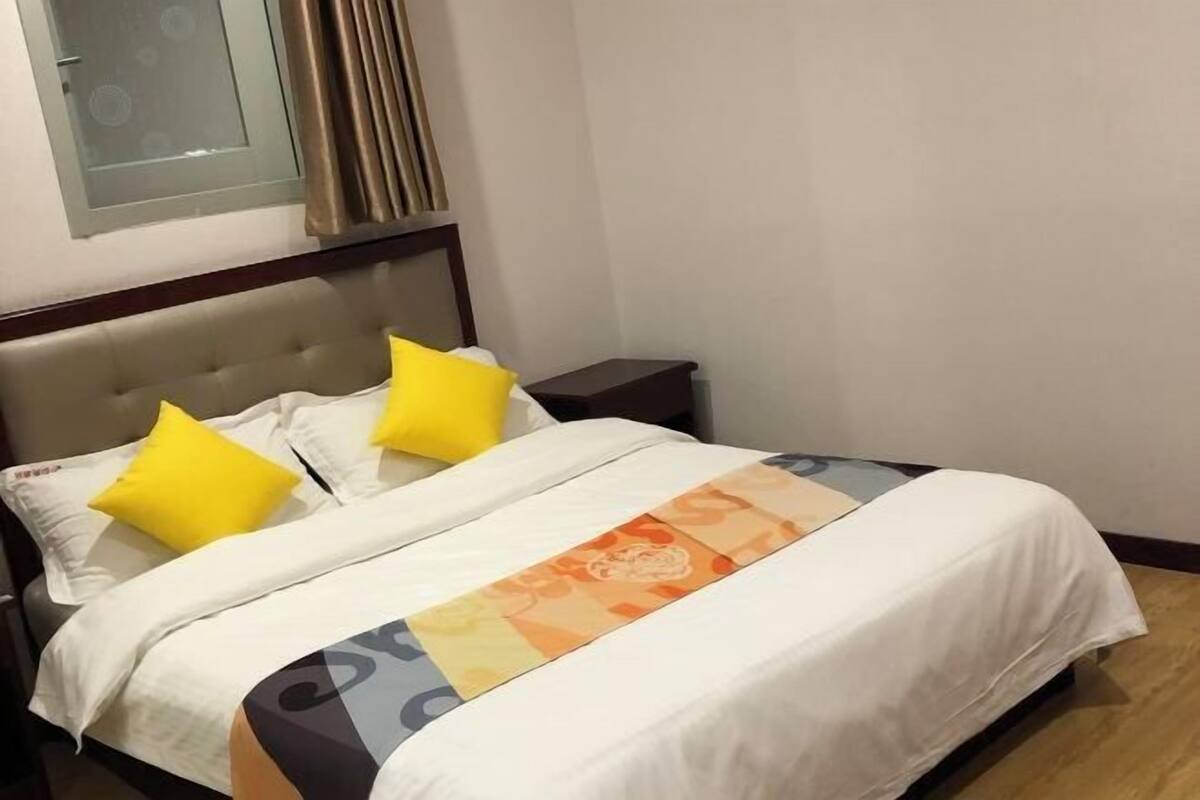A bed with a white and orange patterned bedspread, two yellow pillows, and a wooden headboard.