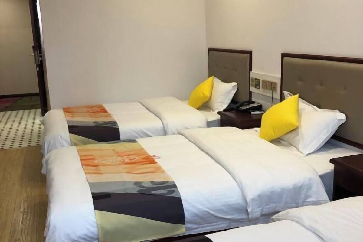 A hotel room with two beds, each with a headboard, white bedding, and a colorful blanket. There is a wooden floor and a door visible in the background.