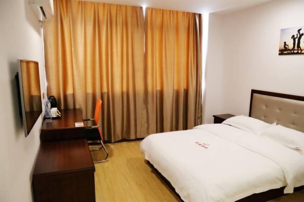A hotel room with a bed, a desk with a chair, a TV, and curtains.