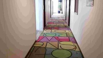 A hallway with a colorful geometric patterned floor, leading to a bright room with a window.