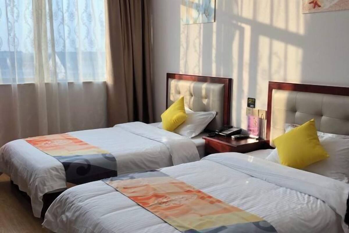 A hotel room with two beds, each with a pillow and a bedside table.