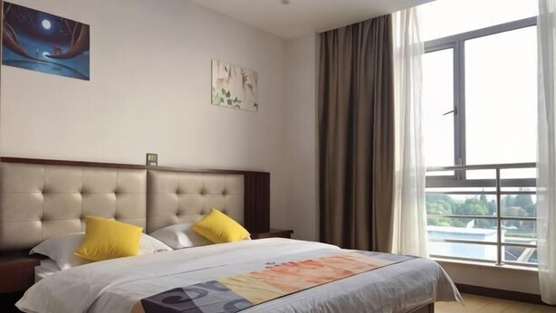 A hotel room with a large bed, two pillows, a nightstand, a window with curtains, and artwork on the wall. - Shell Hotel (Shanghai Zhang Yan Song Jin Street) (Shanghai)