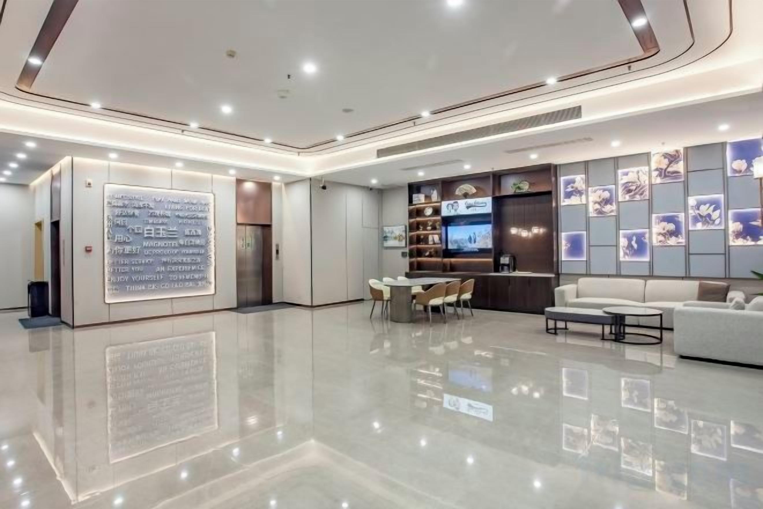 A modern hotel lobby with a polished floor, a reception desk, seating area, and a wall with framed pictures.