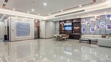 A modern hotel lobby with a polished floor, a reception desk, seating area, and a wall with framed pictures.