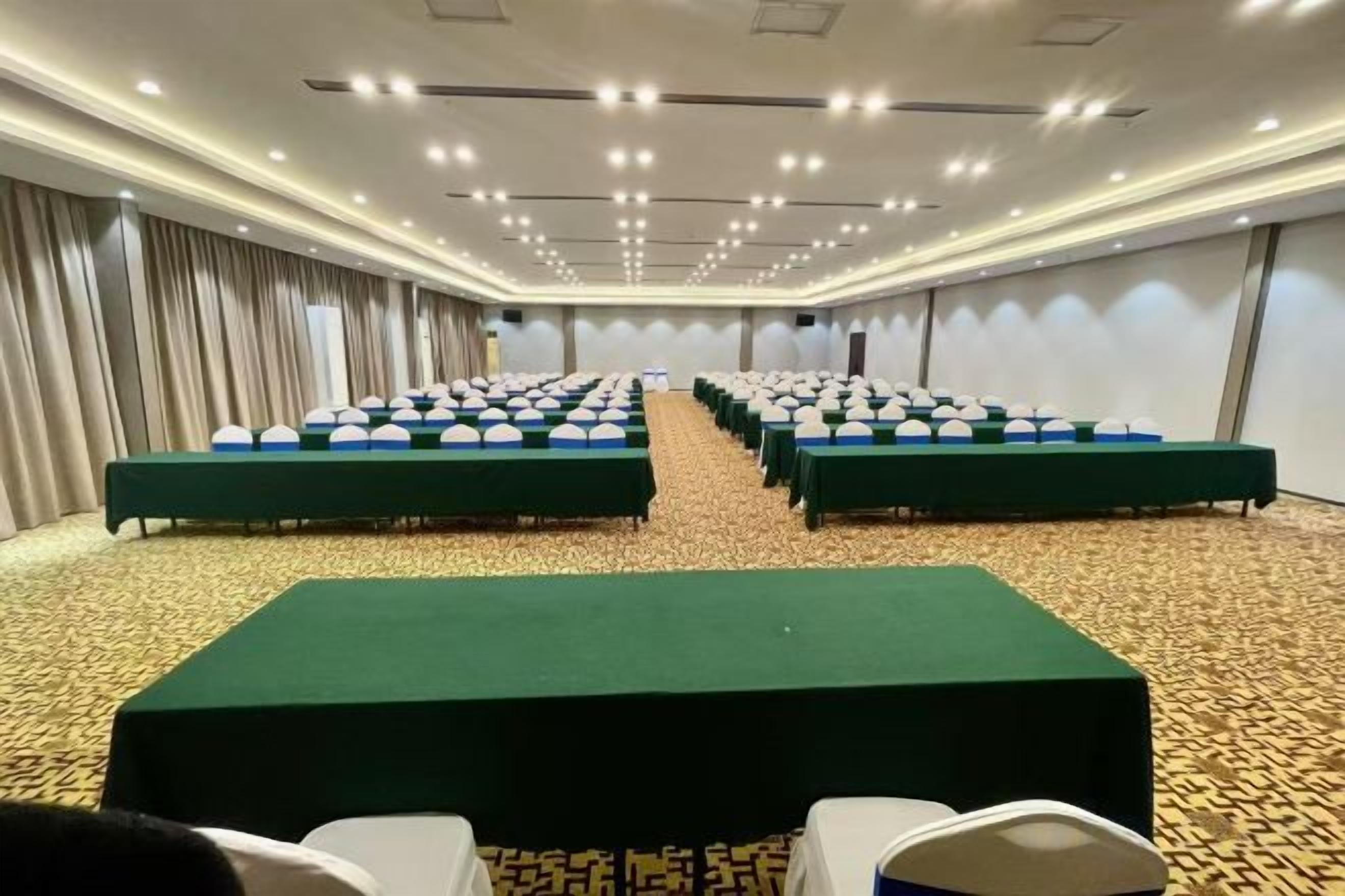 A conference room with rows of tables and chairs, a carpeted floor, and a curtain backdrop.