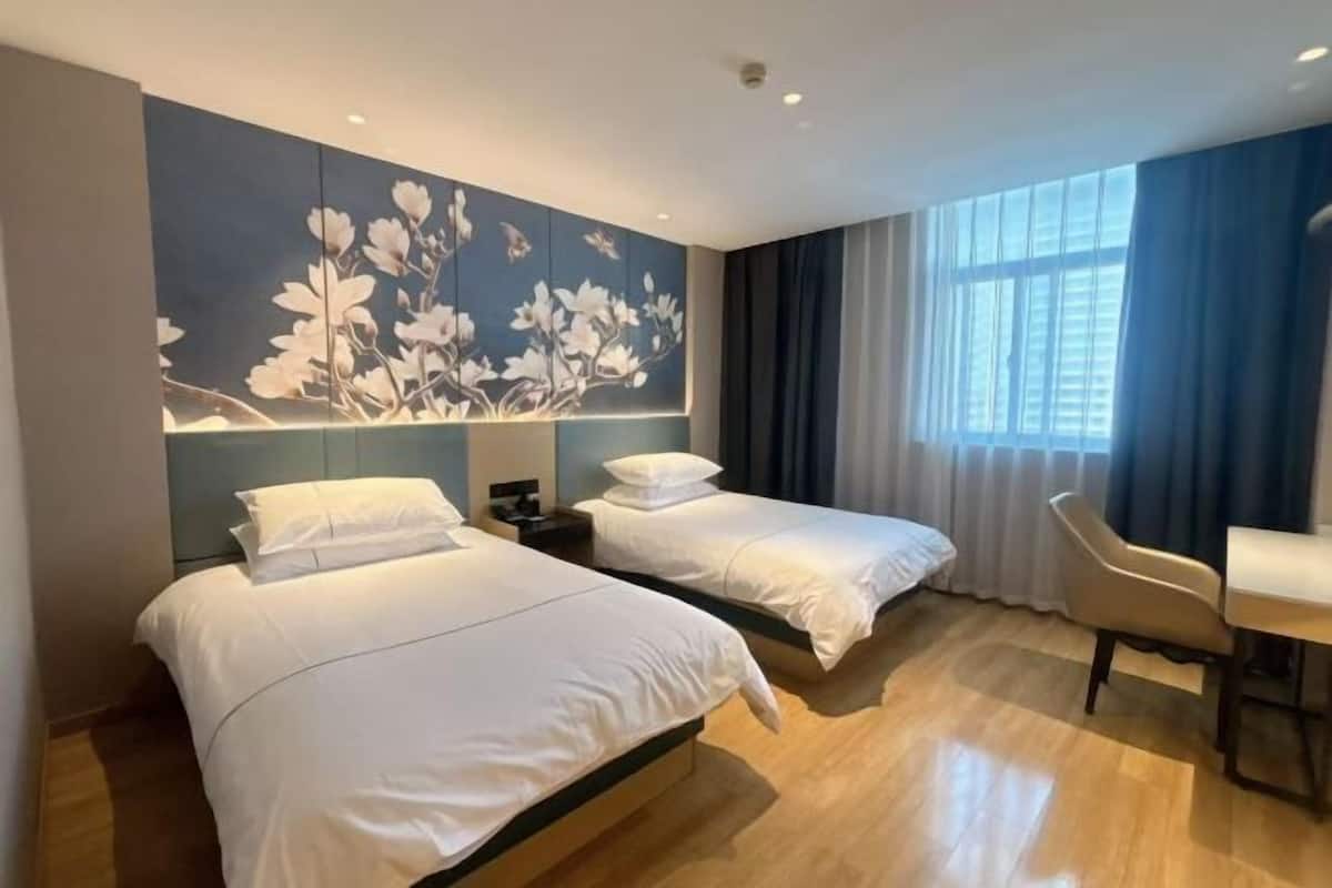 A hotel room with two beds, a desk, a chair, and a large window with curtains.