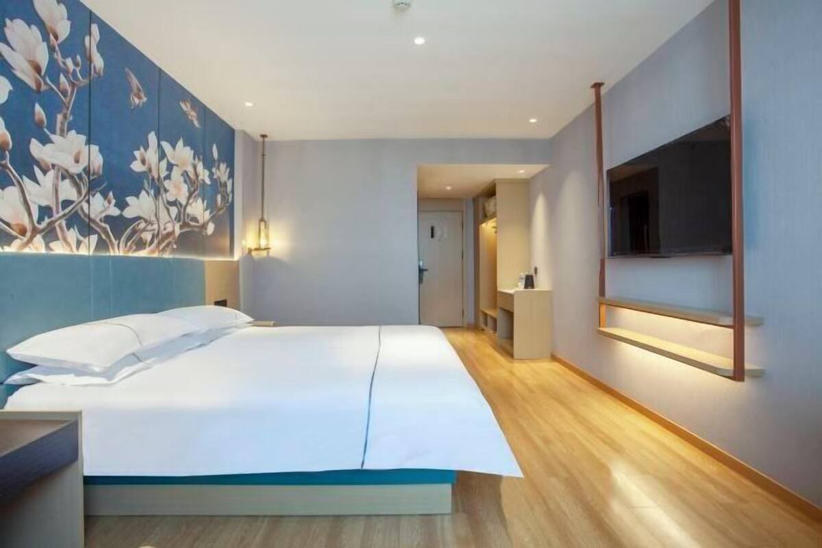 A modern hotel room with a large bed, a wall-mounted TV, and a wooden floor.