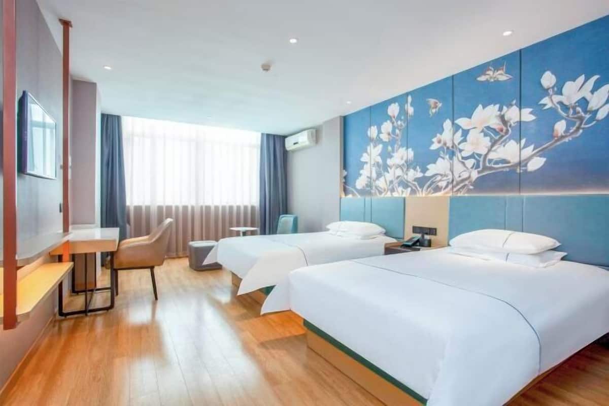 A hotel room with two beds, a desk, a chair, and a large floral wall mural.