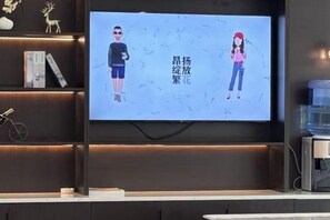 A flat-screen TV mounted on a wall with a shelf below displaying books and a decorative item. - Magnotel Hotel (Yangzhou East High Speed Railway Station) (Yangzhou)