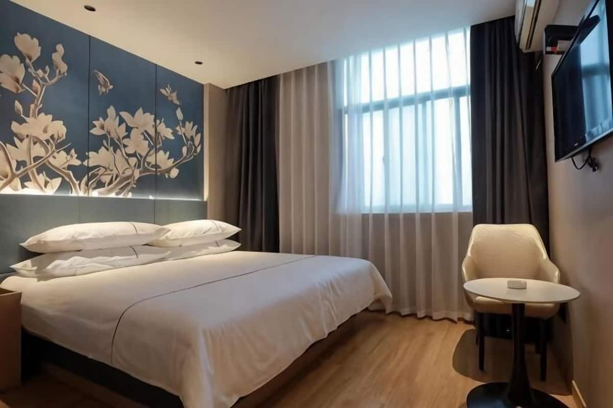 A modern hotel room with a large bed, a small round table, a TV, and a window with curtains.