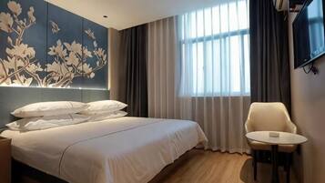 Una habitación de hotel moderna con una cama grande, una mesita redonda pequeña, un televisor y una ventana con cortinas.