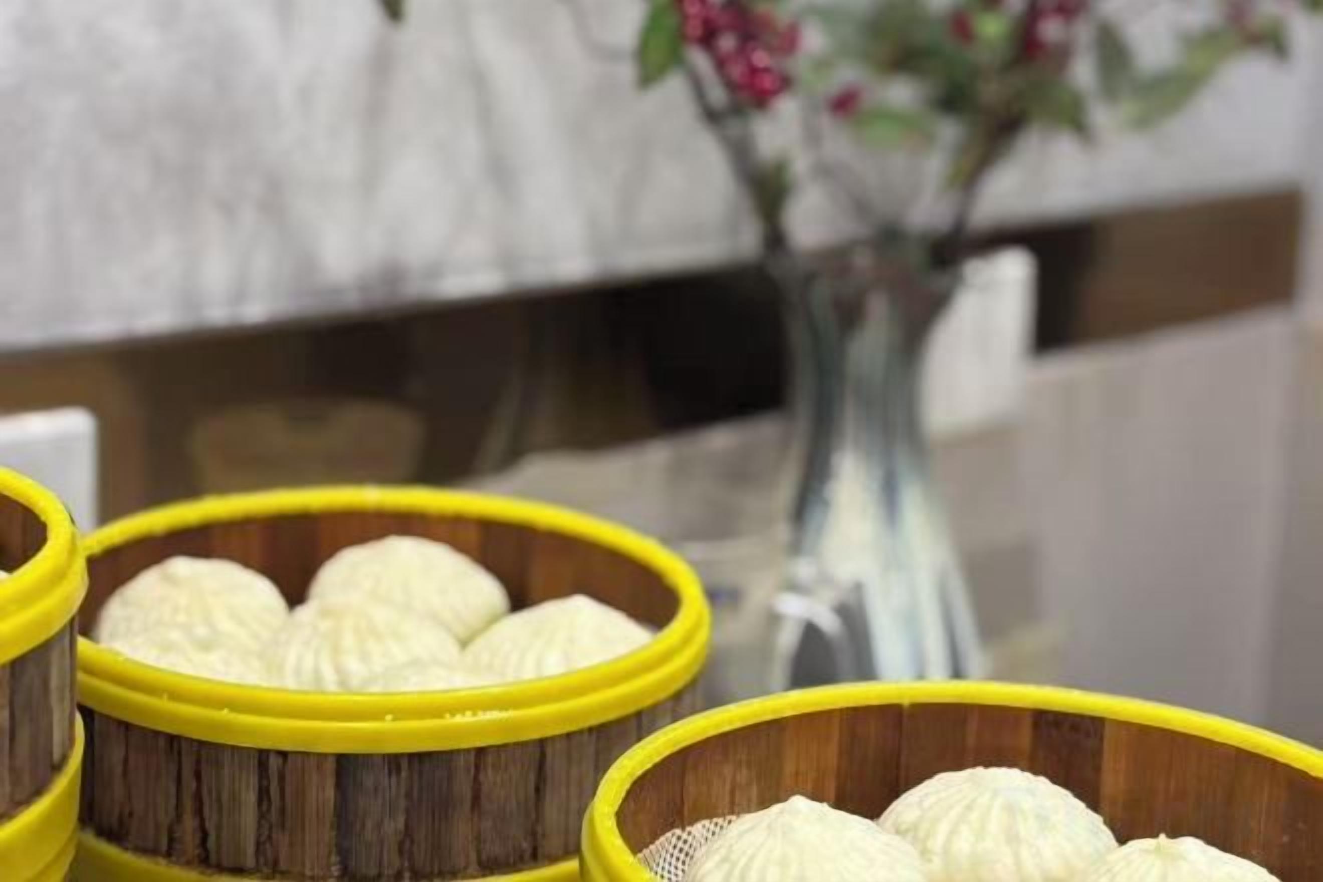 A close-up of yellow baskets containing white items, possibly food, with a blurred background featuring a vase with flowers.