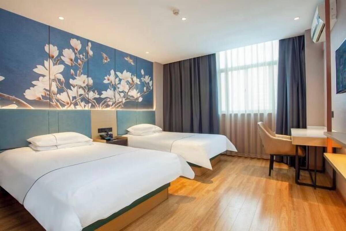 A hotel room with two beds, a desk, and a large window with curtains.