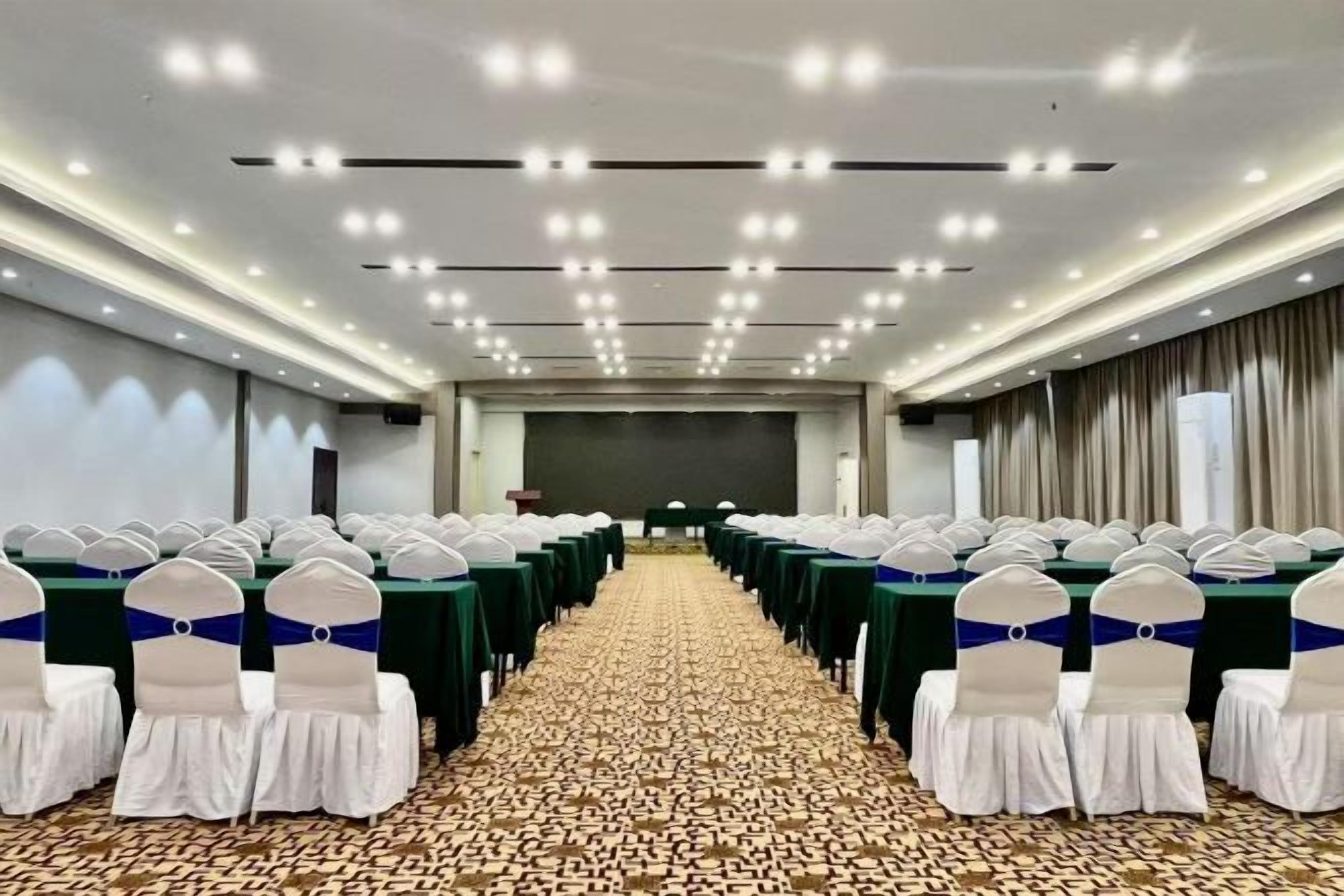 A conference room with rows of tables and chairs, a carpeted floor, and a stage at the front.