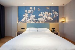 Quarto com cama grande, cabeceira azul e uma obra de arte na parede com flores brancas.