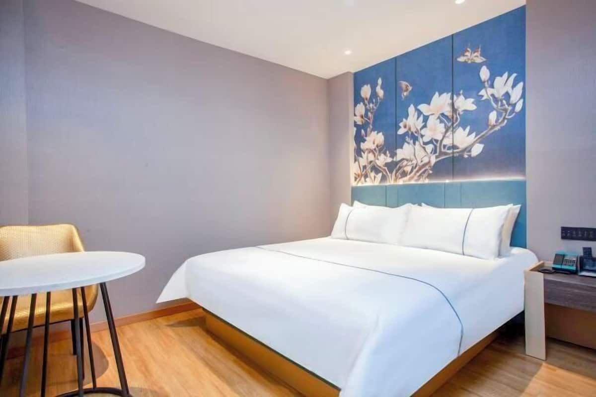 A hotel room with a bed, a round table, and a wall with a floral mural.