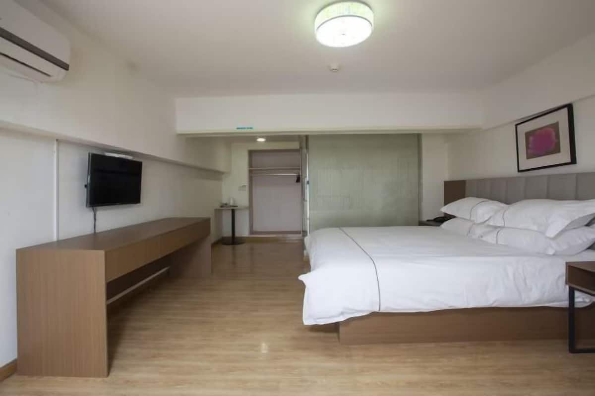 A hotel room with a bed, a TV mounted on the wall, a wooden bench, and a ceiling light.