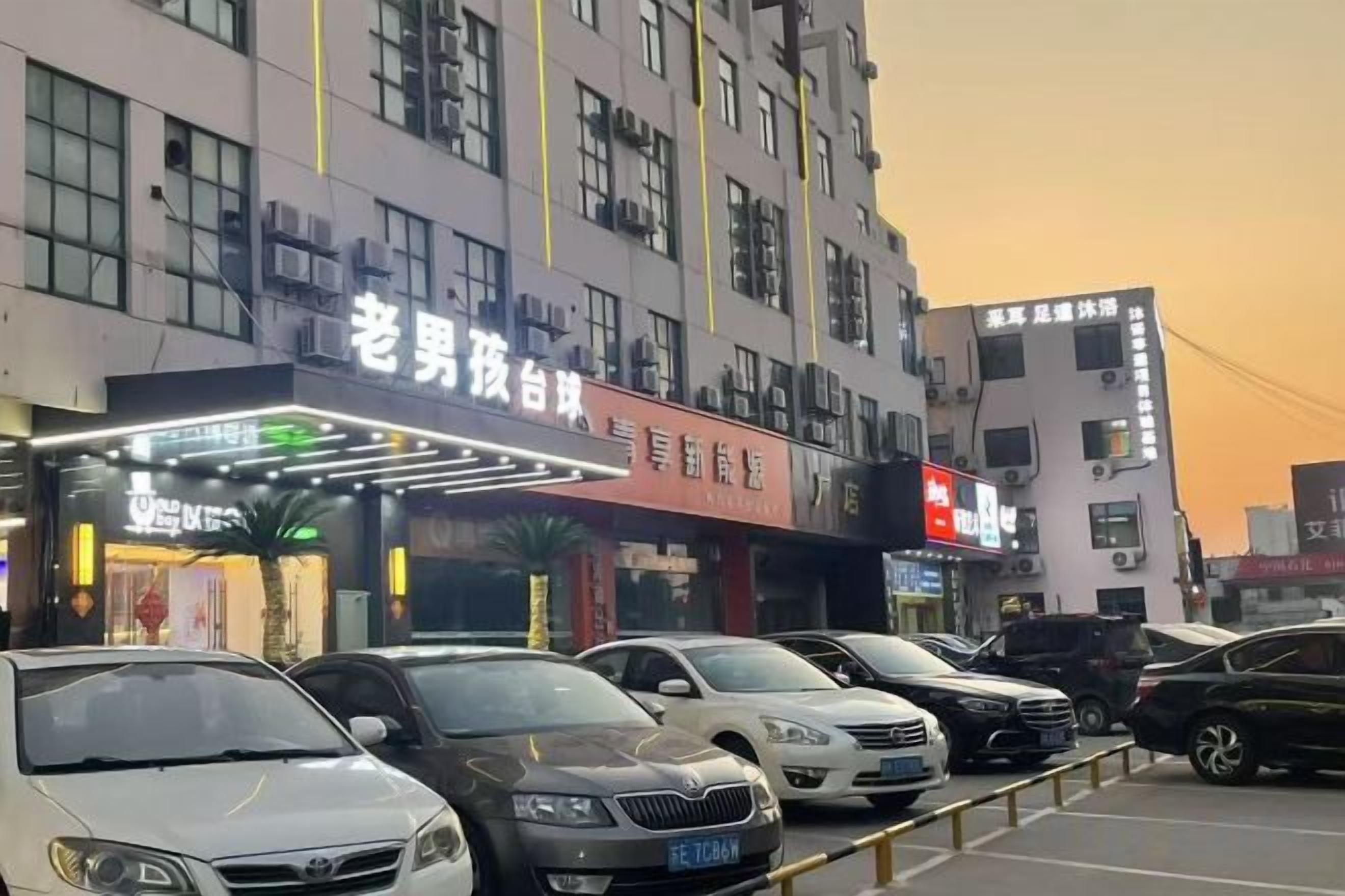 A building with multiple floors, a parking lot with several cars, and illuminated signage.