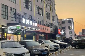Un immeuble à étages, un parking avec plusieurs voitures et une enseigne lumineuse.