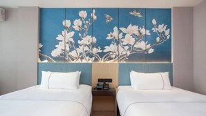 A hotel room with two beds, a blue wall with a floral painting, and a nightstand with a lamp. - Magnotel Hotel (Yangzhou East High Speed Railway Station) (Yangzhou)