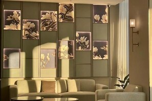 A modern living room with a sofa, armchairs, a coffee table, and a wall with framed floral artwork. - Magnotel Hotel (Yangzhou East High Speed Railway Station) (Yangzhou)