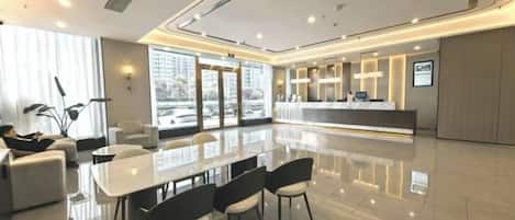 A hotel lobby with a reception desk, seating area, and a large dining table.