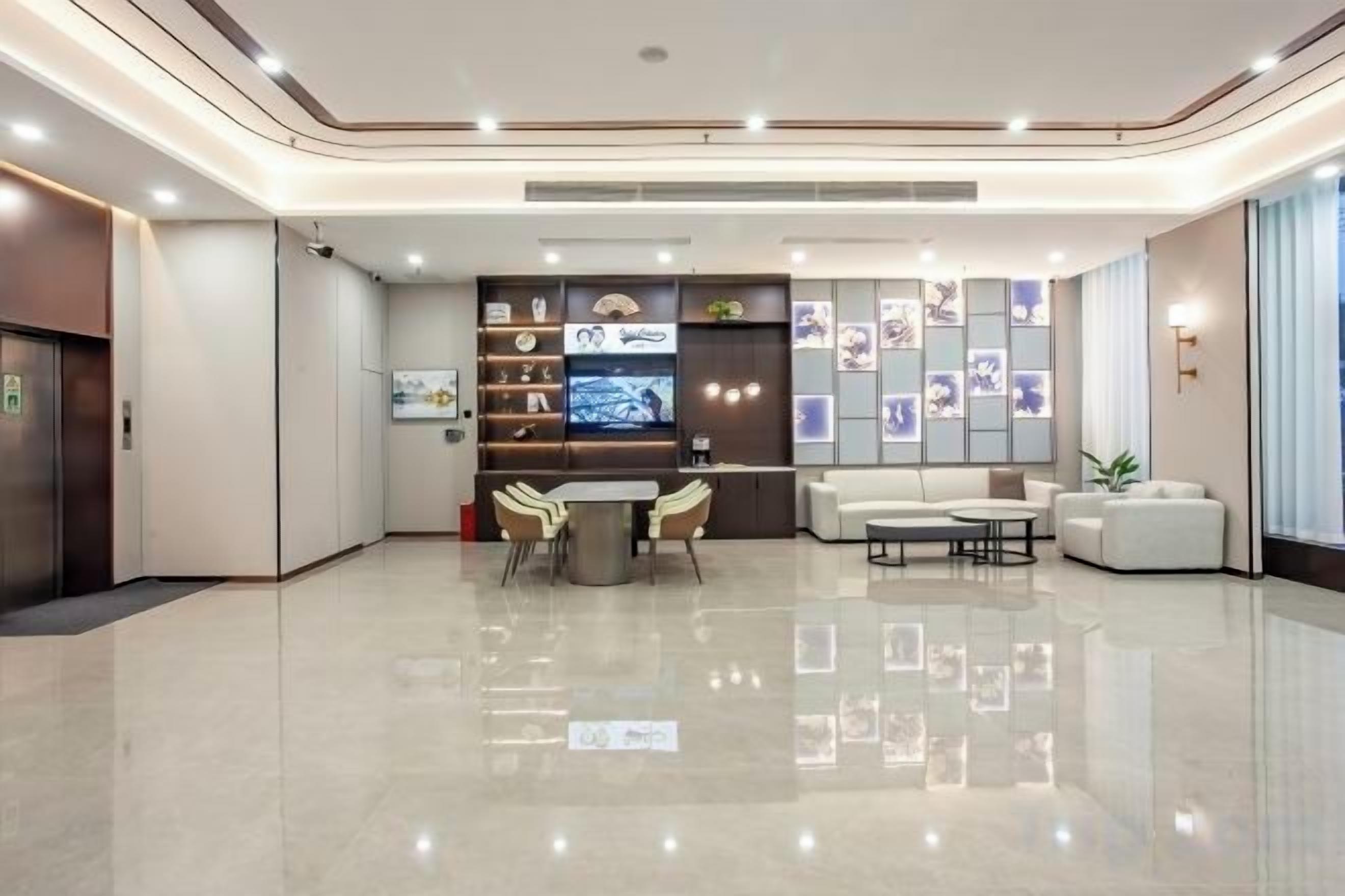 A modern hotel lobby with a reception desk, seating area, and a large TV screen.