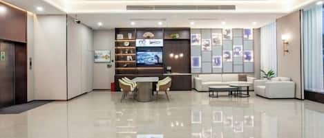 A modern hotel lobby with a reception desk, seating area, and a large TV screen.