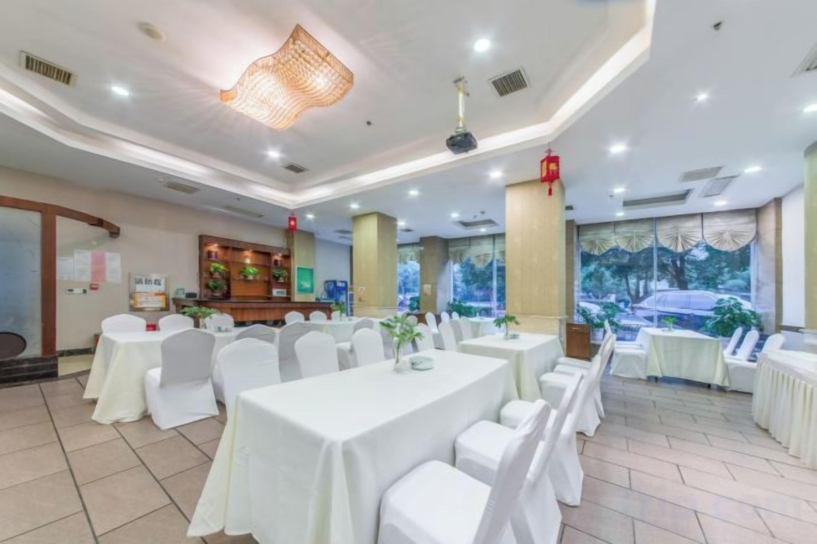 A banquet hall with round tables, white chairs, and a large window with a view of trees.