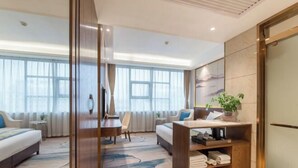 Une chambre d’hôtel moderne équipée d’un lit, d’un bureau, d’une chaise, d’une petite table, d’une bibliothèque et d’une grande fenêtre.