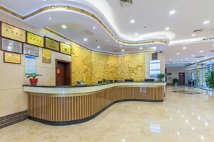 Zona de recepción de un hotel con un mostrador curvo, diplomas enmarcados en la pared y un amplio ventanal.