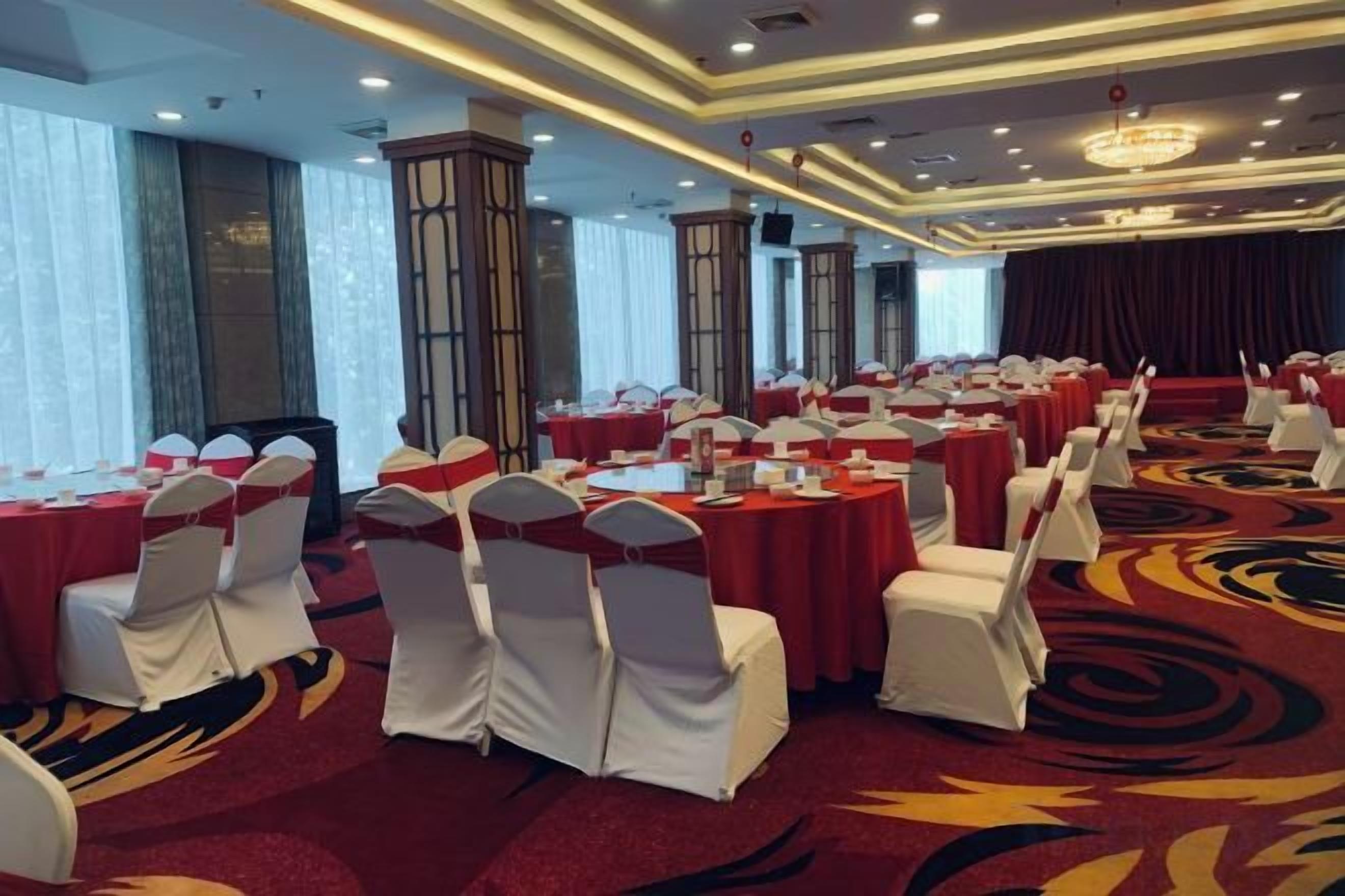 A banquet hall with round tables, white chairs, and red tablecloths.
