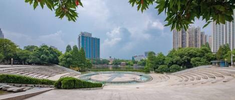 An open plaza with a circular fountain, surrounded by trees and buildings.