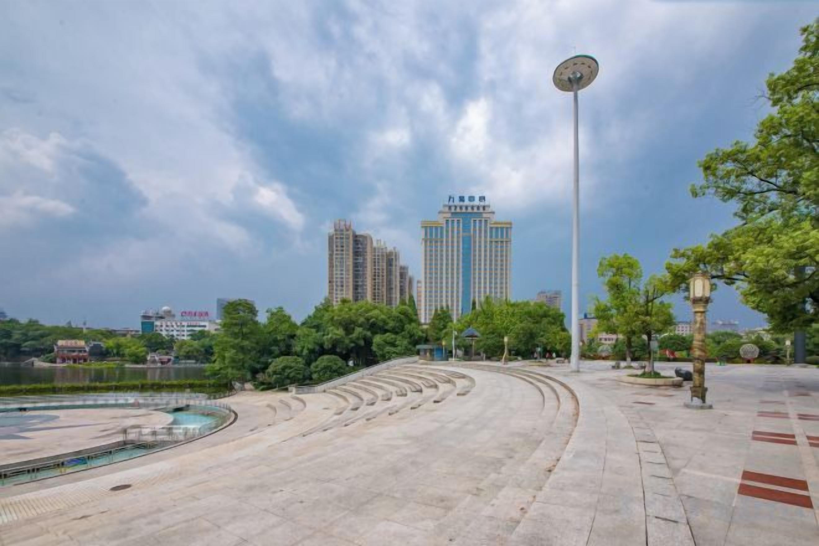 An outdoor amphitheater with tiered seating, a central stage, and a tall lamp post.
