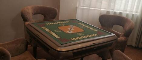A square table with a green and orange board game, surrounded by four brown chairs.