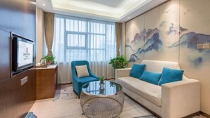 Un salon moderne avec un canapé, un fauteuil et une table basse. Il y a un téléviseur sur le côté gauche et un tableau accroché au mur.