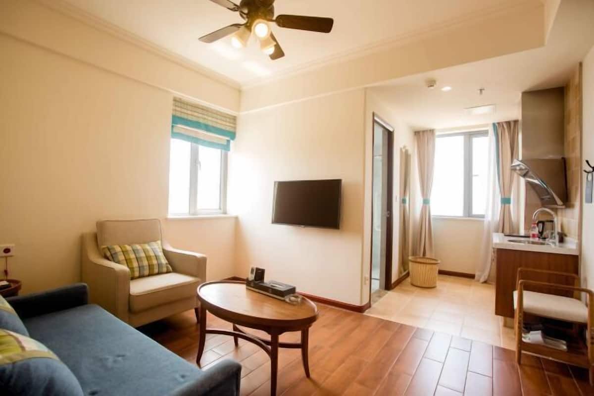 A living room with a sofa, armchair, and coffee table, a flat-screen TV mounted on the wall, and a ceiling fan.