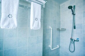 Un baño con azulejos azules, una ducha, un asidero y dos toallas colgadas en un perchero.
