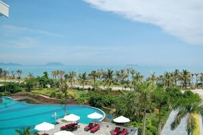 A resort pool with lounge chairs and umbrellas, surrounded by palm trees and a view of the sea. - Zhongan Yinkang Yexiangyuan Hotel (Wenchang)