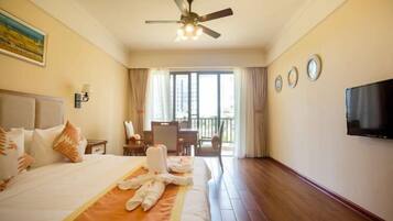 A hotel room with a bed, a ceiling fan, a TV, and a balcony with a table and chairs.