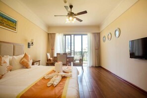 A hotel room with a bed, a ceiling fan, a TV, and a balcony with a table and chairs. - Zhongan Yinkang Yexiangyuan Hotel (Wenchang)