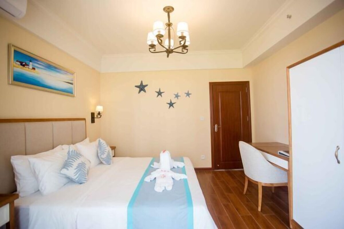 A hotel room with a bed, a desk, a chair, a chandelier, a painting, and star decorations on the wall.