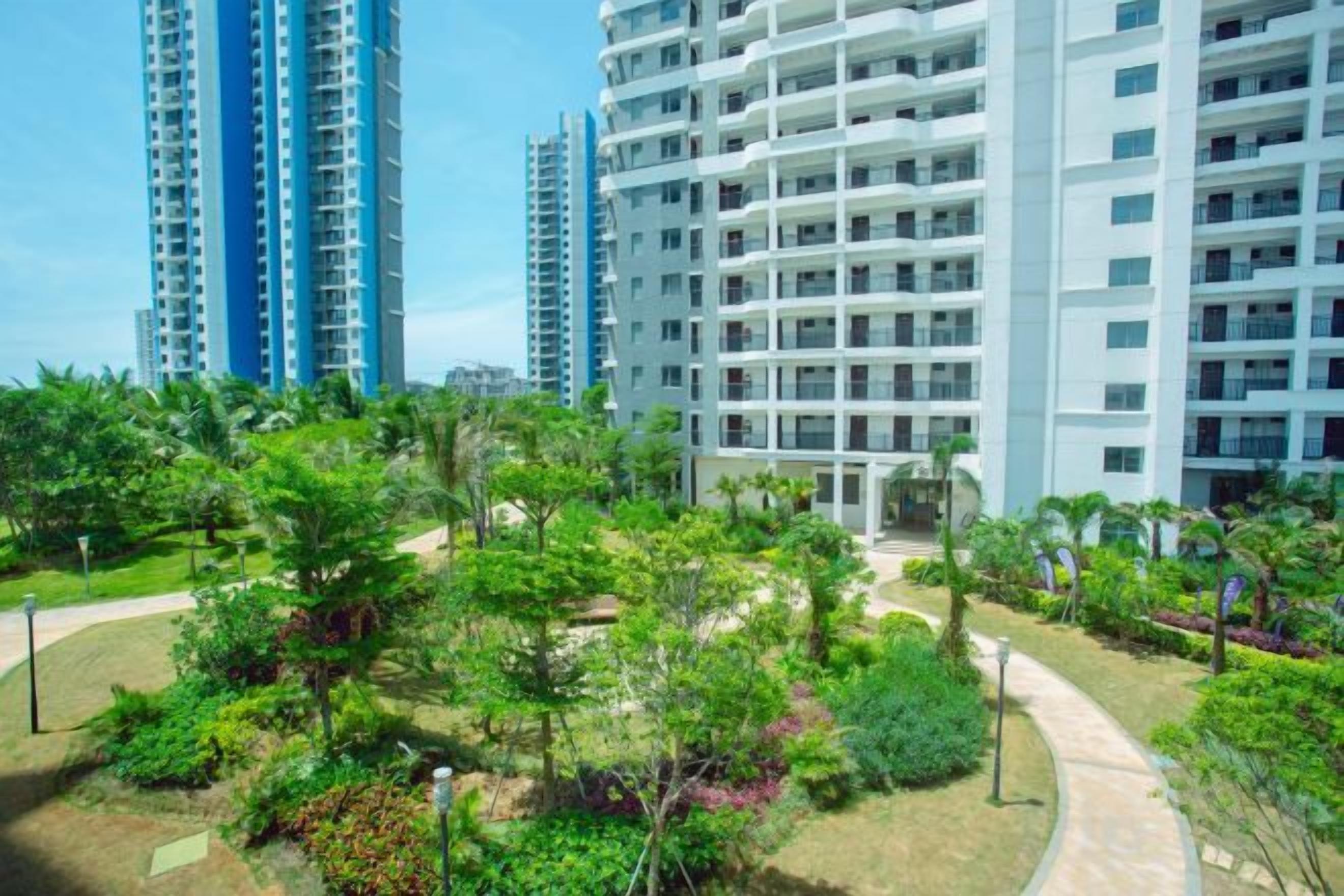 A residential building with multiple floors, surrounded by a landscaped garden with various plants and a pathway.