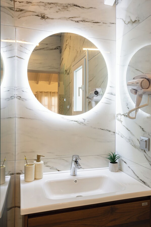 A bathroom with a marble vanity, a round mirror, a hairdryer, and a small potted plant. - La Casa Di Nonna by Corfu Escapes (Corfu)