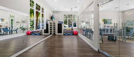 A spacious room with a long wooden floor, large windows, and exercise equipment.