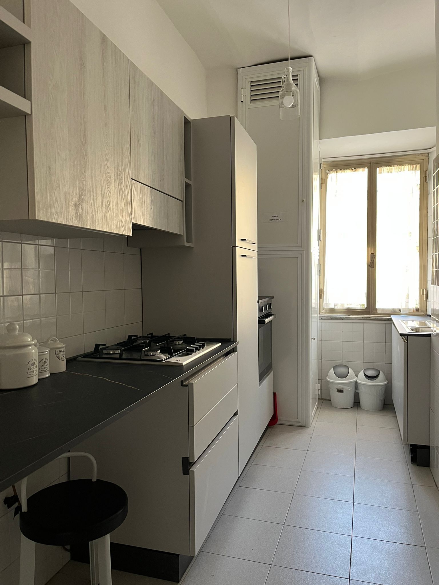 Eine moderne Küche mit weißen Schränken, einem Gasherd und einem Fenster mit Jalousien.
