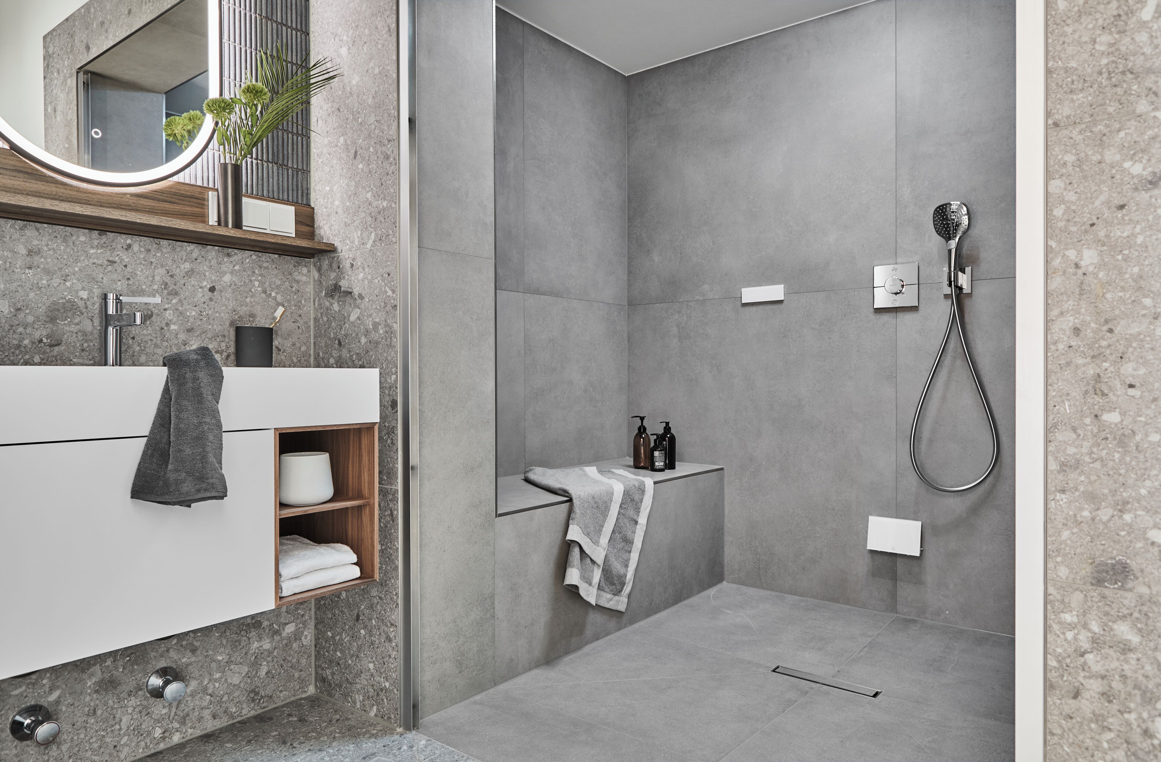 A modern bathroom with a grey-tiled shower, a white vanity with a mirror, and a towel rack.